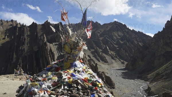 Traditional prayer flags on a stone hill in a wide mountain valley with a dry riverbed, trekking in Ladakh, Stok la, Himalayas, India