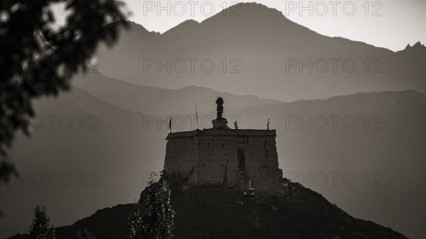 A monastery is majestically perched on a hill with mountains in the background at dusk, Leh, trekking in Ladakh, Himalayas, India
