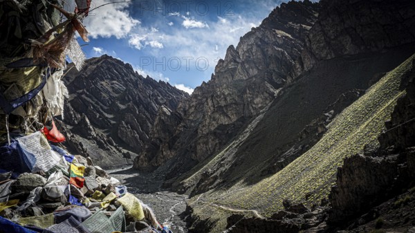 Mountain valley with prayer flags and dry riverbed surrounded by shady mountains, trekking in Ladakh, Stok la, Himalayas, India