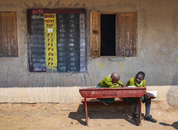 Schoolchildren in school uniform with notebooks sitting at a school desk in front of the classroom, Rushaga, Western Region, Uganda
