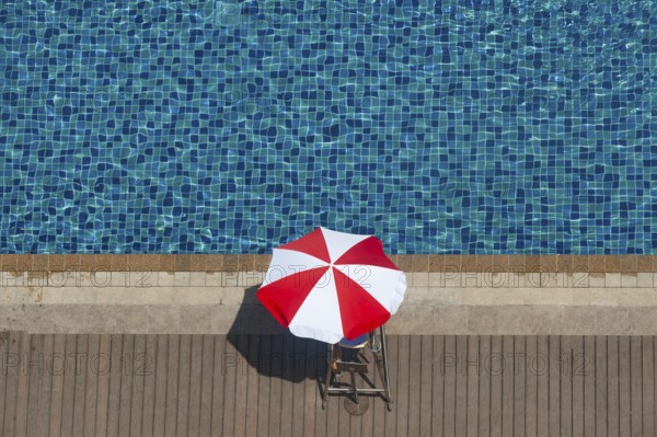 Bright red and white sunshade beside the deep blue water of a hotel pool in the summer time