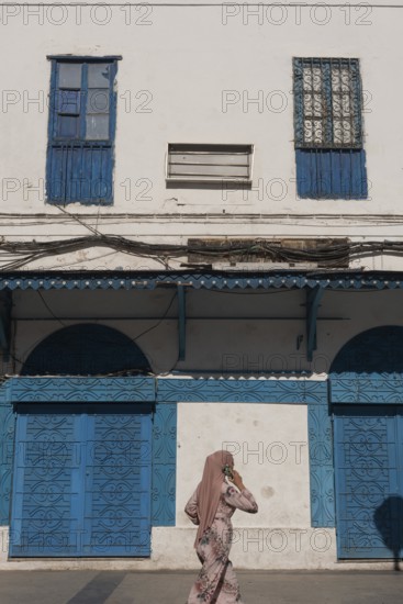 Tunis, Tunisia. 4th May 2024 A Muslim using a cell phone walks past traditional blue coloured architecture in the madina of the Tunisian capital, Tunis