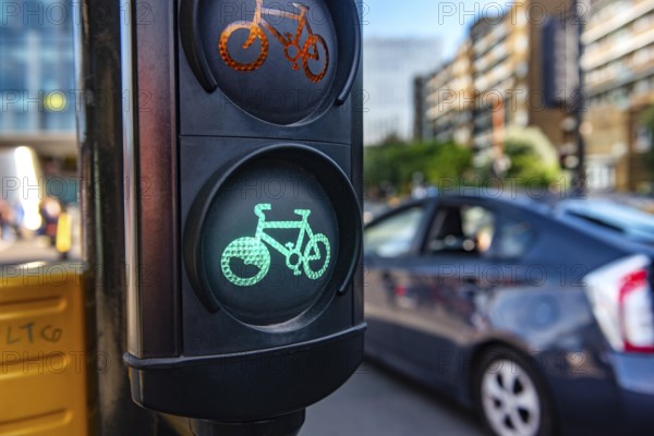 A green cycle lane traffic signal at a junction in a busy London city street with a car passing in the background