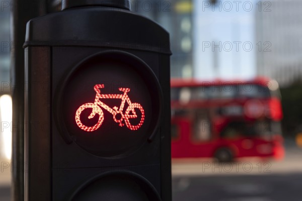 A red cycle lane traffic stop signal at a junction in a busy London city street with a double decker bus passing in the background