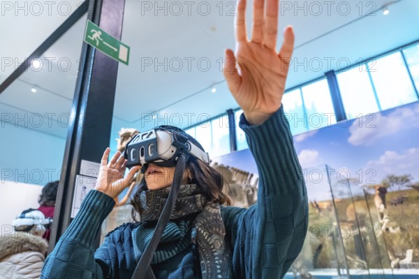 Woman wearing vr goggles, using hand gestures to interact with an immersive digital experience inside a modern museum exhibit, blending learning and technology