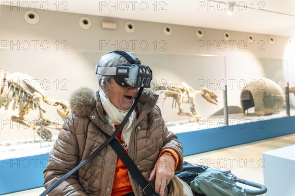 Senior woman wearing a vr headset with an open mouthed, delighted expression experiencing immersive educational fun amid dinosaur fossil exhibits in a modern natural history museum
