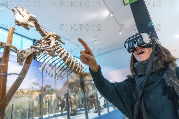 Woman experiencing virtual reality in a natural history museum, interacting with a dinosaur skeleton exhibit through advanced augmented reality technology, pointing with excitement
