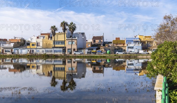 El palmar fishing village houses and palm trees mirrored in the calm albufera lake under a vivid blue sky, traditional waterfront architecture in valencia, spain