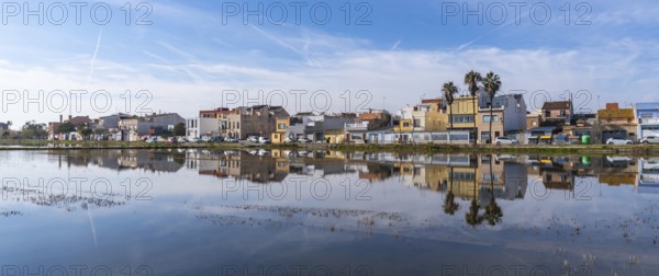 Traditional houses of el palmar fishing village reflecting perfectly on the calm water surface of an albufera rice field, showcasing spanish rural landscape and architecture under a blue sky