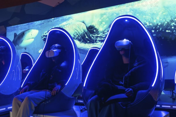 People wearing virtual reality headsets enjoying an immersive deep sea experience while sitting in futuristic individual pods with glowing blue lights in an entertainment center