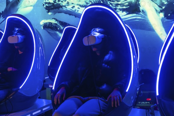 Young woman experiencing a virtual reality underwater whale and shark simulation, sitting in a futuristic vr capsule with neon lights and a large blue screen displaying sea creatures