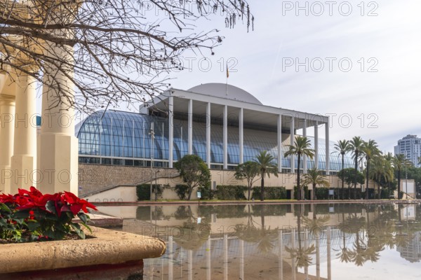 Palau de la musica, a modern concert hall featuring a glass facade and white columns, reflecting on a calm water pond surrounded by palm trees in turia gardens, valencia, spain