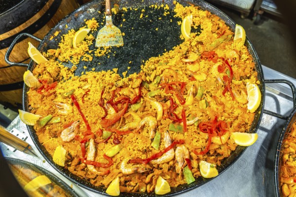 Vibrant yellow rice paella with shrimp, peppers, and lemon wedges preparing in a large traditional pan, emphasizing authentic spanish mediterranean cuisine
