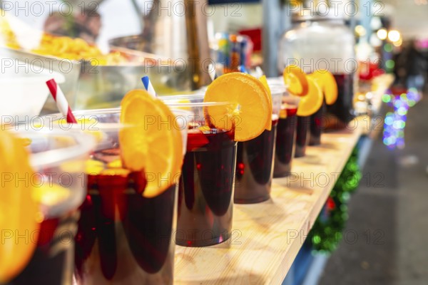 Refreshing sangria beverages served in plastic cups with vibrant orange garnishes and red and blue straws, lined up on a wooden counter at a spanish street market