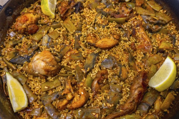 Authentic valencia paella cooking in a wide shallow pan, showcasing flavorful rice, seasoned chicken, green beans, artichokes, and a touch of lemon, representing iconic spanish gastronomy