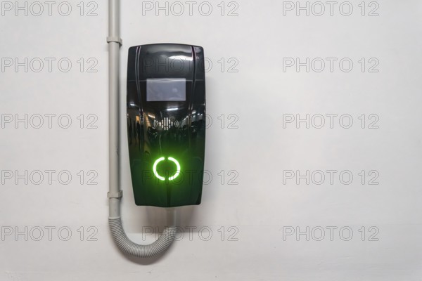 Electric vehicle wallbox charger mounted on a white wall in valencia, spain, glowing bright green to indicate active or ready charging, symbolizing sustainable urban mobility