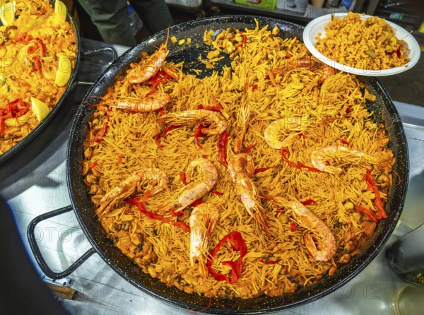 Large paella pan presenting fideua, a traditional spanish noodle dish from valencia, prepared with prawns, seafood, and bell peppers, showing the rich gastronomic culture