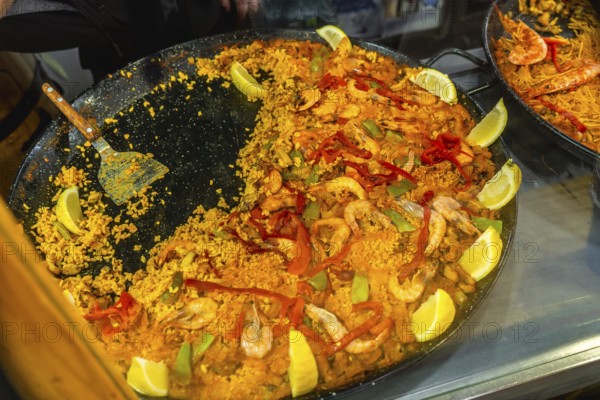 Large traditional spanish seafood paella in a pan with rice, prawns, peppers, mussels, and lemon wedges, showcasing fresh ingredients and authentic mediterranean cuisine