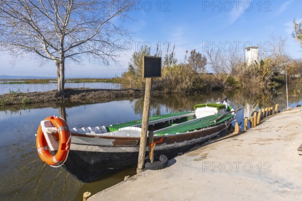 Traditional fishing boat with an orange lifebuoy tied to its bow, moored at a concrete dock beside a calm canal in el palmar, albufera natural park, valencia, spain