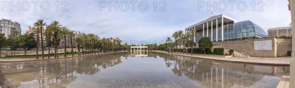 Palau de la musica, a modern architectural landmark, reflecting in the tranquil waters of the turia gardens park, with palm trees lining the long promenade in valencia, spain