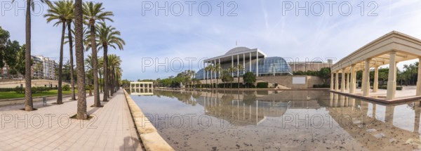 Palau de la musica concert hall architecture reflecting in a calm water pond, surrounded by palm trees and landscaped gardens on a sunny day in valencia, spain