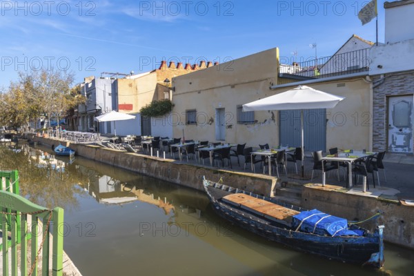 El palmar fishing village showcasing a narrow canal with traditional boats, a row of charming buildings, and an outdoor restaurant terrace with tables and chairs under umbrellas on a sunny day