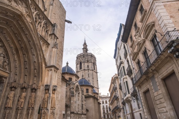 Valencia cathedral with its miguelete tower dominating the skyline, featuring ornate gothic architecture and traditional buildings lining a narrow european street