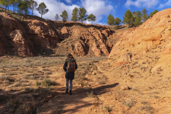 Woman with a backpack hiking through the dry, eroded landscape of las arcillas natural park in teruel, spain, enjoying nature and outdoor activity under a clear sky