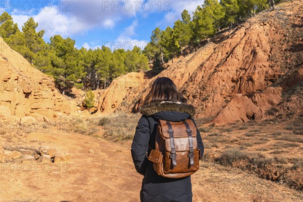 Woman with a backpack exploring the scenic red clay canyons and erosion features of las arcillas natural park, enjoying an active outdoor adventure in the natural landscape
