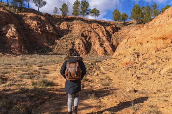 Woman backpacker exploring desert landscape with unique red clay formations and pine trees under a clear blue sky in las arcillas natural park, teruel, spain