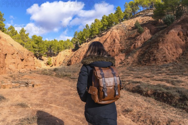 Woman with a leather backpack walking along a dirt path through the striking geological formations of las arcillas natural park in teruel, spain, enjoying nature and outdoor adventure