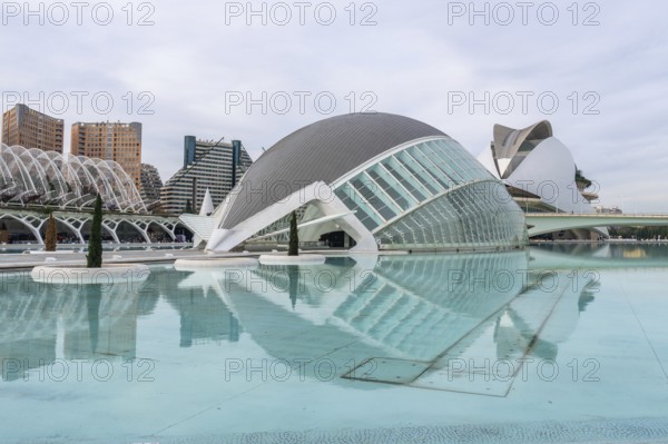 Hemisferic building reflecting in turquoise lagoon at the city of arts and sciences in valencia, spain, surrounded by futuristic, avant garde structures and cloudy sky
