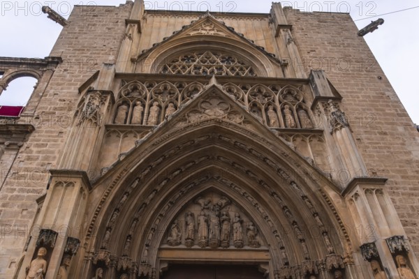 Intricate gothic doorway of valencia cathedral showcasing ornate stone carvings, statues and decorative reliefs on the historic puerta de los apostoles facade, spain landmark
