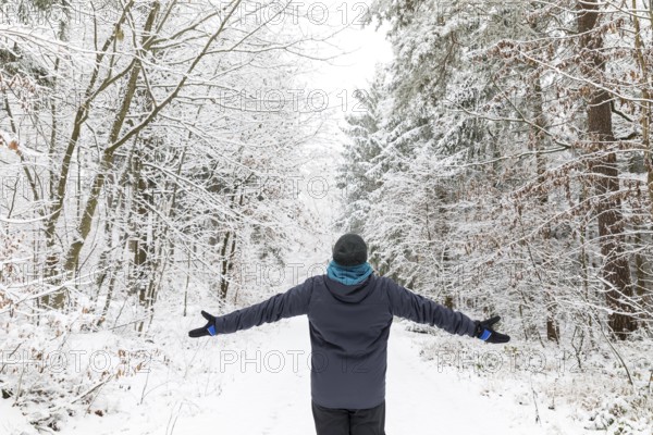 Man from behind standing with arms spread out in snowy winter forest, Tharandter Forest, Saxony, Germany