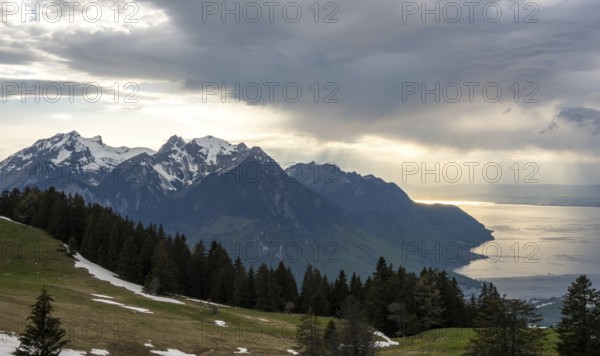 Snow-capped alpine peaks frame Lake Geneva under a dramatic cloudy sky Sunlight casts golden hues on the water, blending rugged mountain beauty with serene lake reflections