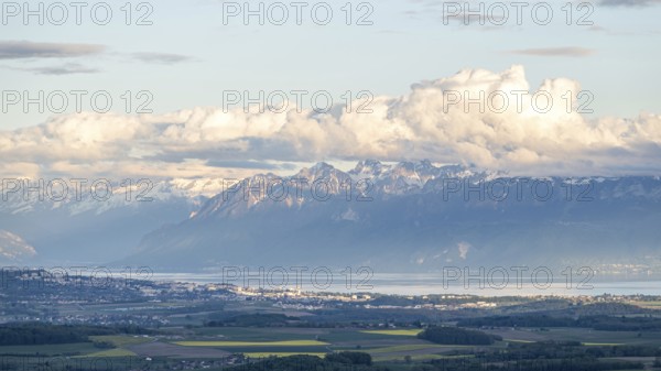 Lake Geneva stretches along the base of towering alpine mountains, with fluffy white clouds casting shadows over the valley A peaceful rural view of Swiss natural beauty