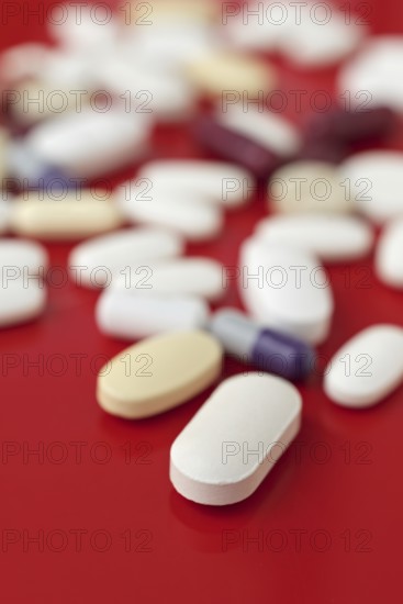 A close-up image of various medical tablets scattered on a bright red background, highlighting different shapes and sizes in a health-related context