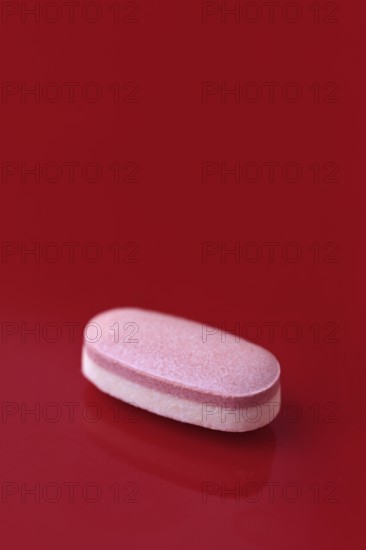 A single pink tablet placed centrally on a vivid red background, conveying a bold contrast that highlights the pharmaceutical's shape and texture