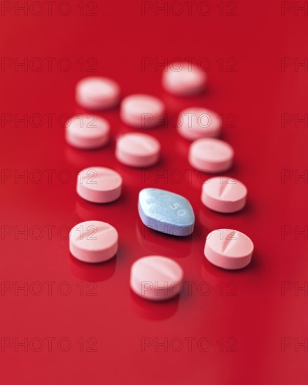 An image featuring a collection of pink tablets scattered on a striking red background, with a single distinct blue tablet marked 50