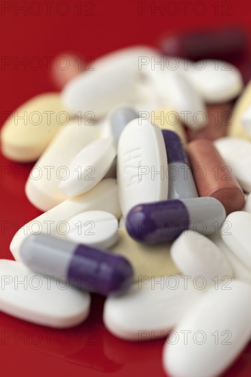 A close-up image showcasing a variety of medical pills and capsules in white, purple, and red colors scattered on a vibrant red background, emphasizing their shapes and colors