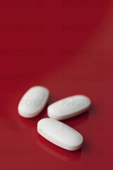 A minimalist image featuring three oblong white tablets, subtly embossed, isolated against a deep red background with a soft focus setting