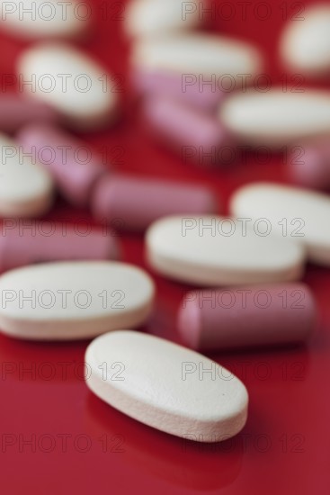 A close-up view of assorted white and pink tablets scattered on a bold red background, highlighting pharmaceutical themes and healthcare