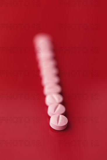 A series of pink medicine tablets aligned diagonally against a stark red background, providing a contrast that emphasizes healthcare and medication themes