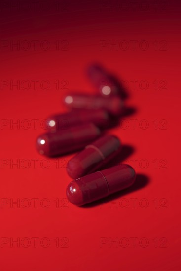 Vibrant image featuring red medical capsules scattered on a uniform red background, creating a monochromatic effect
