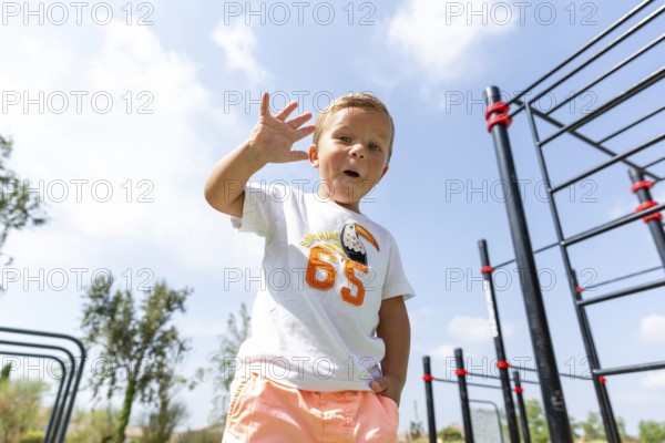 A cheerful child waves at an outdoor playground on a sunny day Wearing a casual outfit, he embodies the joy and excitement of childhood, surrounded by blue skies