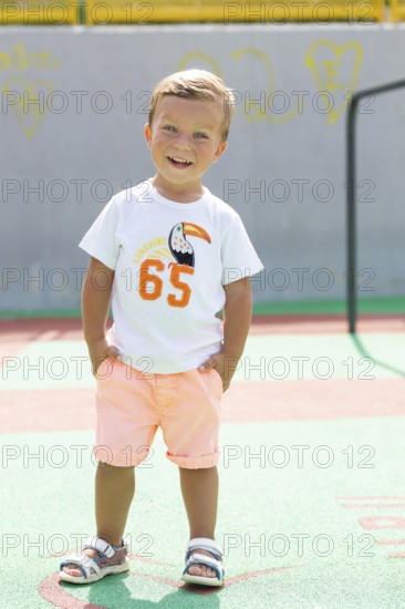 Cheerful young boy with hands in pockets smiling brightly on a sunny day He wears a casual outfit, standing confidently on a colorful outdoor playground