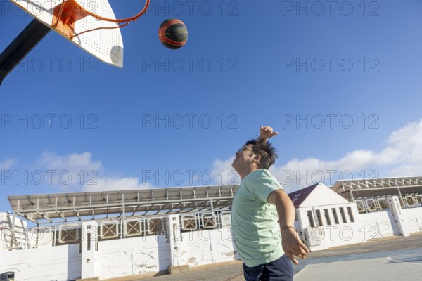Teenager with Down syndrome playing basketball outdoors, emphasizing sports, captured in an open environment, promoting an active and joyful lifestyle