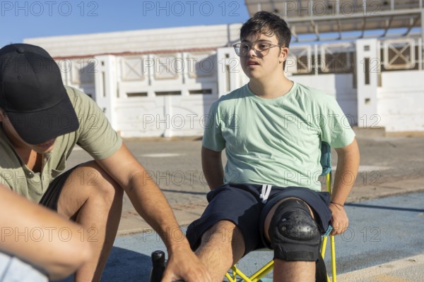 A teenager with Down Syndrome has knee pads adjusted by a family member, preparing for skateboarding on a sunny day The scene highlights inclusion, care, and encouragement