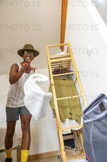 A joyful LGBTQIA+ man enthusiastically packs for holiday travel. Surrounded by clothes and essentials, they radiate excitement and pride, ready for a new adventure