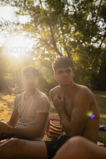 Two young men relax near a serene lake during summer, basking in the golden sunlight filtering through the trees